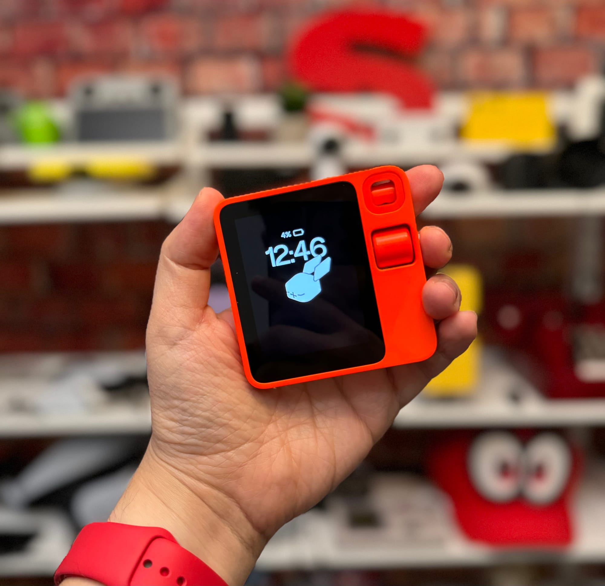 Image of hand holding the Rabbit R1. The time is displayed on the screen. 