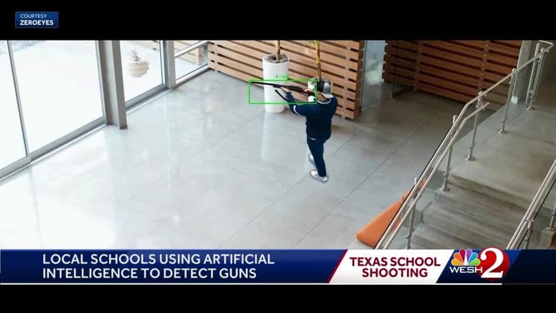 News story freeze frame. Man with rifle is on screen. News chyron says "Local schools using artificial intelligence to detect guns."