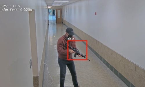 Man with a rifle in a hallway. Detection picks up the firearm and places a red box over it. 